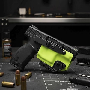 May include: A black handgun with a neon green holster is displayed on a black surface. Several bullets and a bottle of gun oil are also visible. The gun is angled, showcasing its design and features.