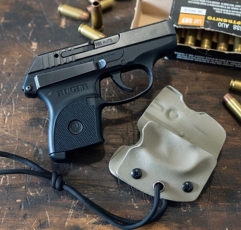 May include: A black Ruger 9mm pistol with a black grip and a tan holster. The pistol is next to a box of ammunition and several loose bullets. The pistol has the word "Ruger" printed on the side.