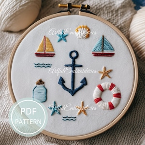 May include: Embroidered nautical design in a wooden hoop. Features a blue anchor, sailboats, starfish, seashell, life preserver, and a bottle. The text "PDF PATTERN" is in a circle at the bottom left. The design is on white fabric.