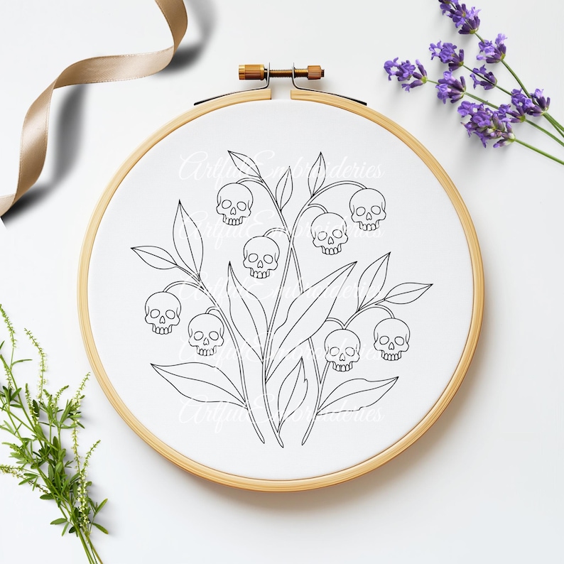 Puede incluir: Un bastidor de bordado circular de madera que contiene tela blanca con un dise&ntilde;o de arte lineal negro de flores de lirio de los valles donde las flores en forma de campana son reemplazadas por peque&ntilde;as calaveras humanas, rodeadas de hojas y tallos verdes.