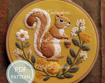 Puede incluir: Un bordado detallado de una ardilla sosteniendo una bellota, en un aro de madera. La ardilla es marrón y blanca, rodeada de flores y hojas bordadas sobre un fondo amarillo. El texto "Artful Embroidieries" es visible.