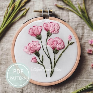 Puede incluir: Primer plano de un patrón de bordado rosa de claveles en un aro de bordado de madera. El patrón está sobre tela blanca e incluye tallos y hojas verdes. El texto "Artful Embroideries" es visible en la tela.