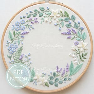 May include: Embroidered floral wreath in a wooden hoop. The design features light blue, lavender, white, and green flowers and foliage. The text "Artful Embroideries" is visible. A PDF pattern is also available.
