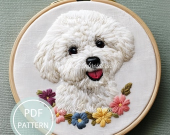 May include: A circular wooden embroidery hoop containing a white fabric panel with a detailed thread-stitched portrait of a fluffy white dog. The dog has dark eyes and a pink tongue. A colourful floral arrangement sits below the dog's chin.