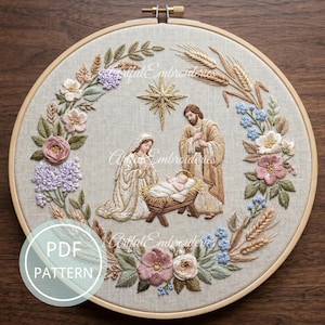 May include: A circular embroidery hoop containing a nativity scene stitched on light beige fabric. The design features a central gold star above a figure kneeling beside a manger with a baby, and a standing figure, all framed by floral wreaths.