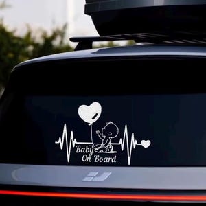 May include: White vinyl car decal featuring a baby holding a heart-shaped balloon. The design includes a heartbeat line and the text "Baby On Board". The decal is designed to be applied to a car window.