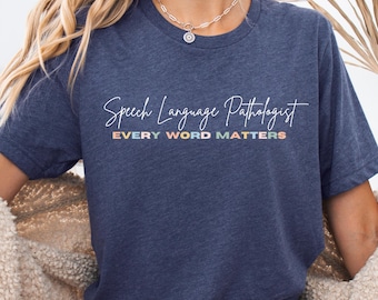 Può includere: T-shirt blu navy con la scritta "Speech Language Pathologist" in corsivo bianco. Sotto, il testo "EVERY WORD MATTERS" è stampato a colori arcobaleno. La maglietta è a girocollo.