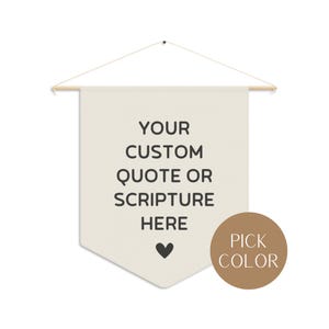 May include: A beige canvas wall hanging with a wooden dowel at the top and a string for hanging. The canvas has the text "YOUR CUSTOM QUOTE OR SCRIPTURE HERE" printed on it with a small heart below the text. A brown circle with the text "PICK COLOR" is in the lower right corner of the image.