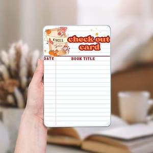 Könnte beinhalten: Eine rechteckige weiße Karte mit Retro-Design, mit dem Text "check out card" in Rot und Orange. Die Karte hat Linien für "Date" und "Book Title" und ein dekoratives Banner mit Kürbissen und den Worten "Kindle Girlie".