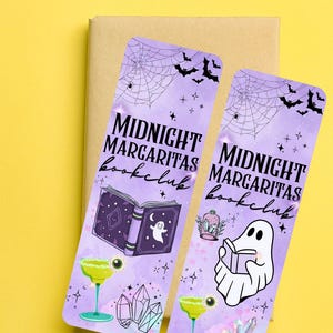 Puede incluir: Dos marcapáginas morados con el texto "MIDNIGHT MARGARITAS bookclub". Uno presenta un libro abierto con un fantasma, el otro un fantasma leyendo un libro. Ambos tienen murciélagos, telarañas y copas de margarita.