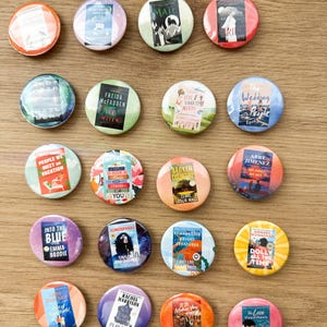 May include: A collection of twenty circular pin-back buttons, each featuring a miniature book cover illustration. The designs include various titles and authors such as Project Hail Mary, The Witch, Love and Other Words, and The Love Hypothesis.