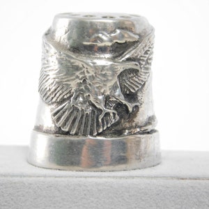 Puede incluir: Dedal de plata con diseño de águila. El águila está en vuelo con las alas extendidas. El dedal tiene un acabado liso y pulido.