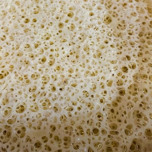 May include: Close-up of a light brown, foamy surface with a textured, bubbly pattern.