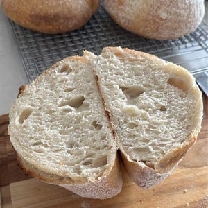 May include: A close-up of a freshly baked loaf of bread sliced in half, revealing a light and airy crumb. The bread has a golden brown crust and is lightly dusted with flour.
