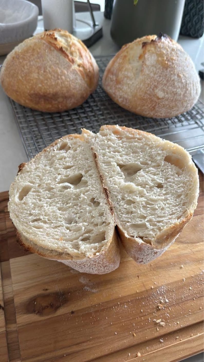 May include: A close-up of a freshly baked loaf of bread sliced in half, revealing a light and airy crumb. The bread has a golden brown crust and is lightly dusted with flour.