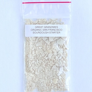 May include: A clear plastic bag with a red zipper closure contains a white sourdough starter. The bag has a white label that reads "Great Grandma's Organic San Francisco Sourdough Starter."