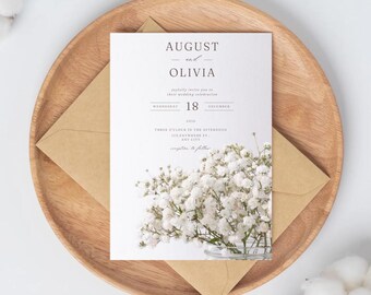 May include: A wedding invitation featuring the names "August and Olivia" with the date "December 18". The invitation is on a white background with a floral arrangement and a kraft paper envelope, presented on a wooden plate.