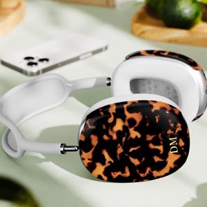 May include: White and tortoiseshell headphones with the initials "DM" on the ear cup. The headphones are on a light green surface, with a white phone and other objects in the background.