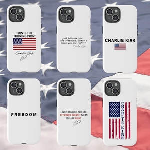May include: White phone cases with various designs. One features the text "THIS IS THE TURNING POINT" with an American flag and signature. Another says "just because you are offended, doesn't mean you are right." Other cases say "FREEDOM" and "CHARLIE KIRK."
