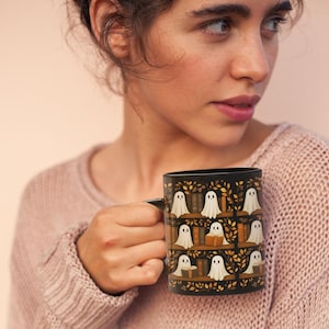May include: Black ceramic mug featuring a repeating pattern of white ghost figures on bookshelves with books and autumn leaves. The mug has a black handle and a black interior. The design is set against a black background.