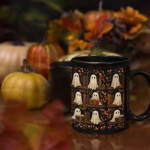 May include: Black ceramic mug featuring a repeating pattern of white ghost figures on bookshelves, with autumn leaves and pumpkins in the background. The mug has a black handle and is likely for hot beverages.