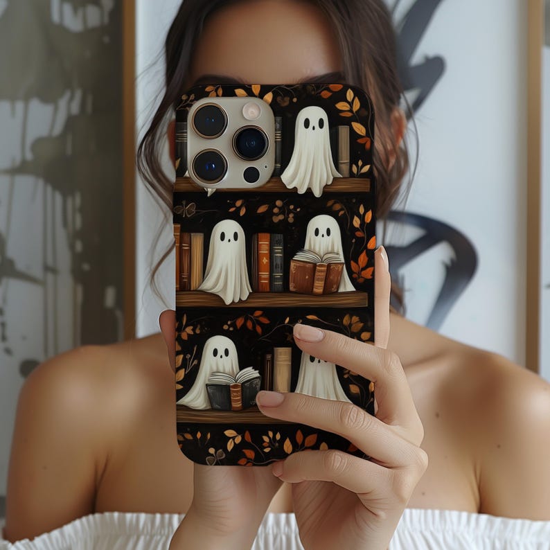 May include: A black phone case featuring a bookshelf design with cartoon ghosts and books. The ghosts are white with black dot eyes, and some are reading books. The background has autumn leaves.