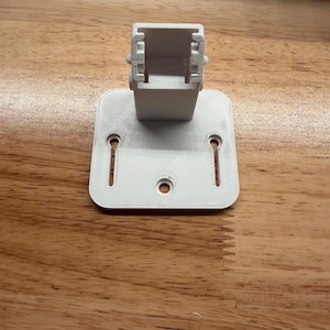 May include: A white 3D-printed bracket with a rectangular top and a square base. The base has three holes for mounting. The bracket is designed to hold an object. The item is made of plastic.
