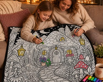 Peut inclure: Une grande couverture de coloriage rectangulaire en tissu présentant une illustration au trait noir et blanc d'un cottage entouré de fleurs, de champignons et de lanternes suspendues, avec certains éléments partiellement colorés en jaune et rose.