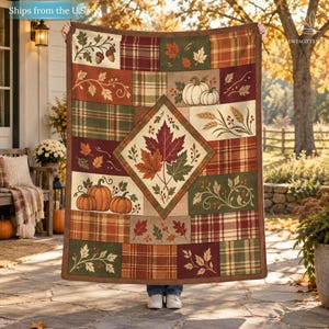 Pode incluir: Uma manta retangular com um design de patchwork apresentando motivos de outono, incluindo abóboras, folhas de bordo, espigas de trigo e padrões xadrez em tons de laranja, castanho, verde e creme, centrada com um grande painel em losango.