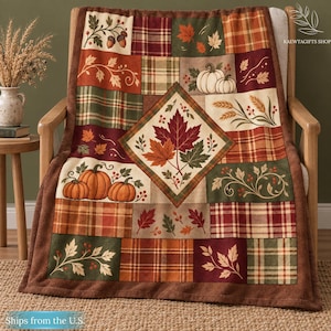 May include: A throw blanket featuring a patchwork design with autumn-themed patterns including pumpkins, acorns, wheat stalks, and maple leaves in shades of orange, brown, green, and cream. The center displays a large diamond-shaped panel.