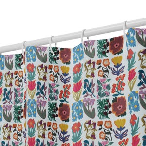 May include: A shower curtain featuring a repeating floral pattern in red, yellow, blue, and purple on a white backdrop. The curtain is suspended from a white rod with white rings, adding a touch of colour to the bathroom.
