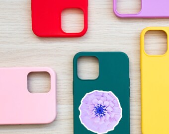 Puede incluir: Cinco fundas para teléfono diferentes, cada una con un color y un diseño diferente. Una funda es rosa, una es roja, una es verde, una es amarilla y una es morada. La funda verde tiene una pegatina de una flor morada.