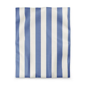 Può includere: Una coperta o un plaid a righe blu e bianche. Le strisce verticali sono uniformemente distanziate, creando un design classico e pulito. Il tessuto appare morbido e leggermente strutturato, con un sottile motivo a onde.