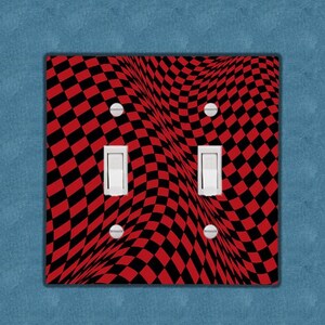 May include: A red and black checkered light switch cover with a wavy pattern. The cover is designed to fit a standard double light switch.