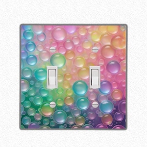 Puede incluir: Una tapa de interruptor de luz con un patrón de burbujas de colores. Las burbujas son iridiscentes y parecen flotar en un fondo de colores arcoíris.