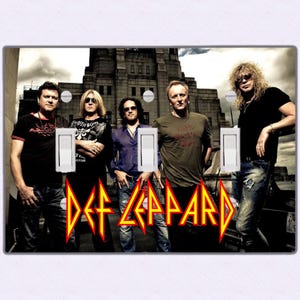 May include: A light switch cover featuring a photo of the rock band Def Leppard. The band members are standing in front of a building with the band's name in large, red letters.