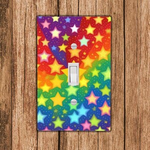 May include: A light switch cover with a rainbow background and yellow stars. The stars are of different sizes and are scattered across the cover.