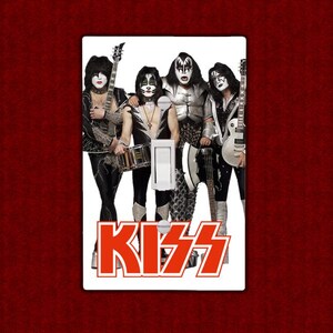 May include: A white light switch cover featuring a black and white image of the rock band KISS. The band members are wearing their iconic makeup and costumes. The word "KISS" is printed in red below the image.