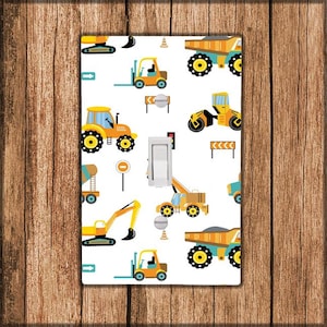 May include: A white light switch cover with a repeating pattern of yellow construction vehicles, including a forklift, dump truck, excavator, and bulldozer. The background is white with black outlines.