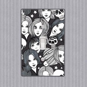 May include: Black and white light switch cover featuring a pattern of stylised faces and skulls. The design is whimsical and spooky.