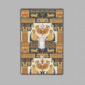 Puede incluir: Cubierta decorativa para interruptor de luz con un patrón repetido de gatos estilizados, columnas y elementos florales en tonos dorados, azul marino y crema. El interruptor blanco está centrado.