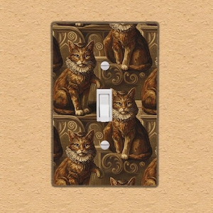 Puede incluir: Una cubierta decorativa para interruptor de luz con un patrón repetido de gatos marrones con collares con volantes. Los gatos están colocados sobre un fondo de detalles arquitectónicos ornamentados. El interruptor es blanco.