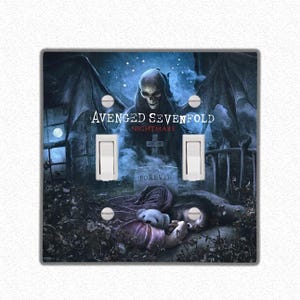 Pode incluir: Uma placa de cobertura de interruptor duplo com uma imagem escura e gótica de uma figura esquelética com asas, uma lápide e o texto "Avenged Sevenfold Nightmare Forever".