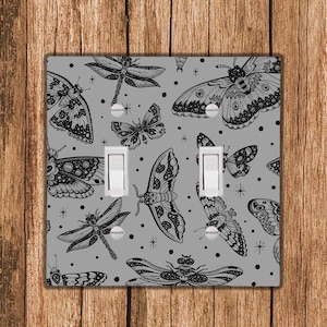 May include: A light gray light switch cover with a black and white pattern of butterflies and dragonflies. The switch cover has two toggle switches.