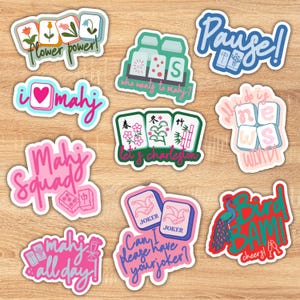 K&ouml;nnte beinhalten: Eine Sammlung farbenfroher Aufkleber mit verschiedenen Designs und Texten zum Thema Mahjong. Die Aufkleber enthalten S&auml;tze wie "Flower Power!", "I love Mahj" und "Mahj Squad". Andere Aufkleber sagen "Pause!", "Bird Bam!" und "Can I please have your joker?"