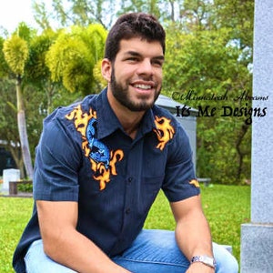 Peut inclure: Un homme portant une chemise à manches courtes bleu foncé avec un motif floral jaune et bleu. Il est assis sur un banc en pierre, les jambes croisées. Il porte un jean bleu et une montre argentée.
