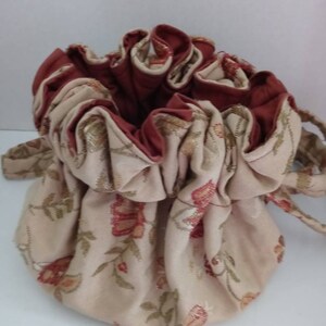 Könnte beinhalten: Eine beige Kordeltasche mit einem Blumenmuster und rotem Futter. Die Tasche ist aus Stoff und hat einen gerafften oberen Rand.