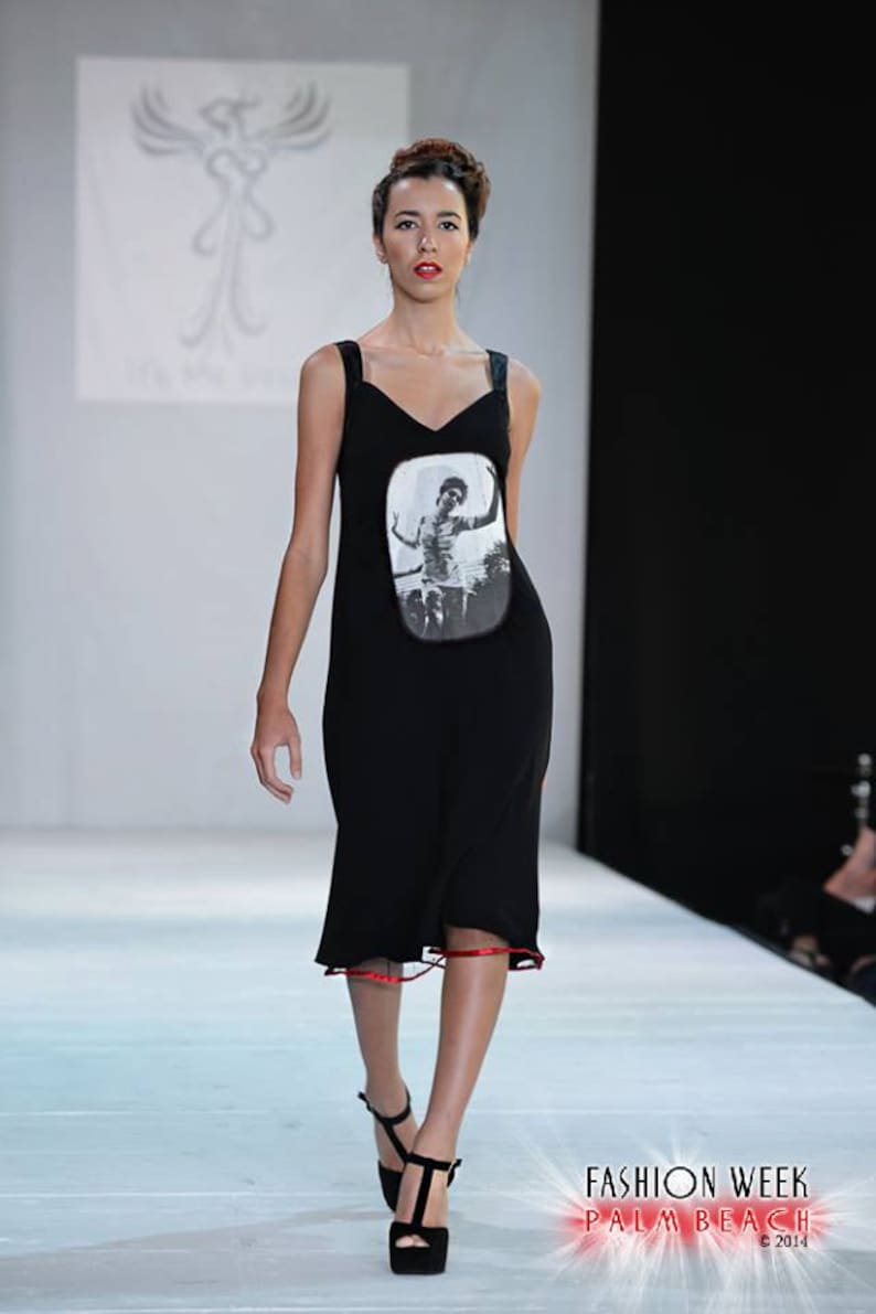 Puede incluir: Una modelo camina por la pasarela con un vestido negro con un estampado fotogr&aacute;fico en blanco y negro de una persona en bicicleta. El vestido tiene un ribete rojo en el dobladillo. La modelo lleva tacones negros.