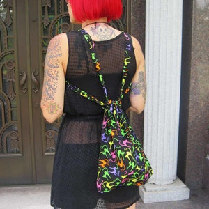 Puede incluir: Un vestido negro con una superposición transparente y una bolsa de estampado de gatos coloridos. La bolsa se lleva como una mochila y tiene correas ajustables.