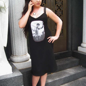 Puede incluir: Una mujer lleva un vestido negro sin mangas con un estampado gr&aacute;fico de una persona con una camisa blanca. El vestido tiene un escote redondo y una silueta ajustada. Lleva tacones negros y tiene el pelo recogido hacia atr&aacute;s.